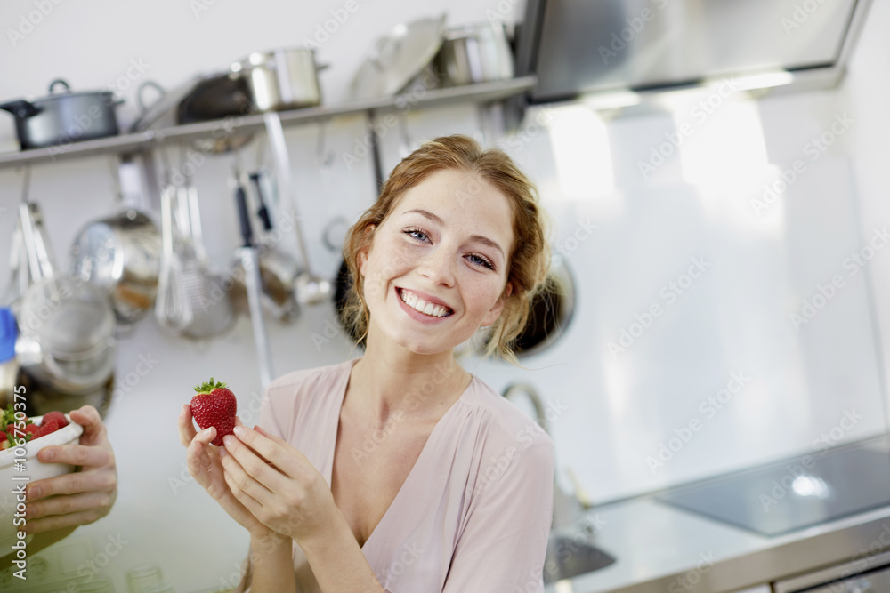 Portrait of happy young woman holding strawberry in kitchen Portrait of happy young woman holding strawberry in kitchen