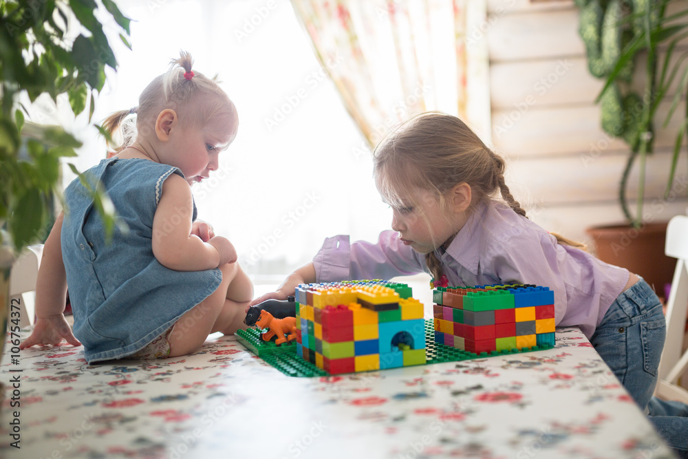 little Caucasian girl sisters playing constructor on a table ,