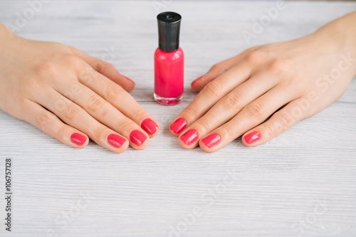 Female hands with red manicure and nail polish bottle on a woode