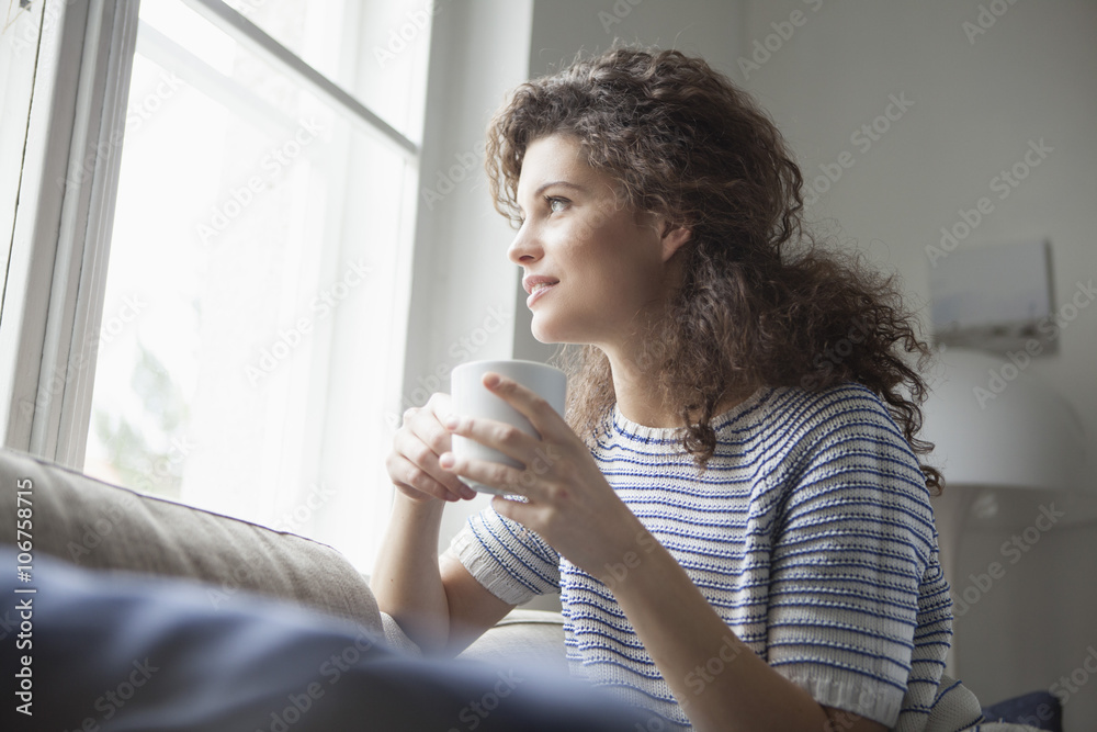 Smiling young woman with cup of coffee looking out of window Smiling young woman with cup of coffee looking out of window