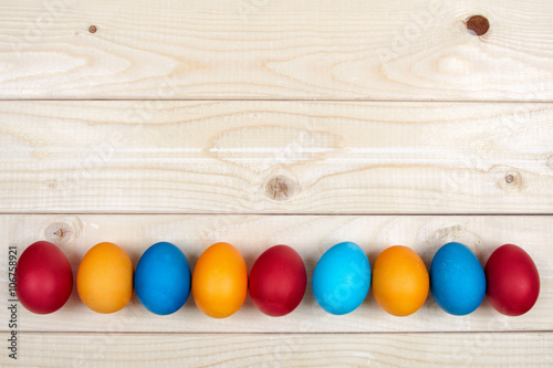Colored Easter eggs decoration line over the light wooden surface as a copyspace festive background composition