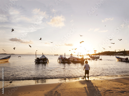 Venezuela, Isla Margarita, Juan Griego, back view of little boy standing at seafront by sunset photo