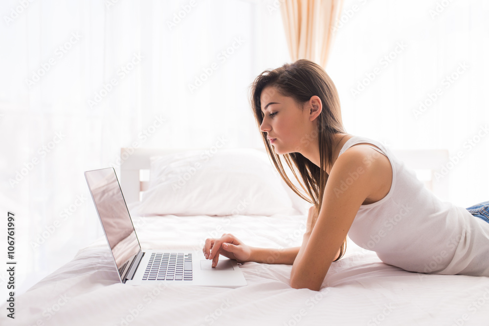 pretty girl looking at laptop monitor while lying on bed in her room pretty girl looking at laptop monitor while lying on bed in her room