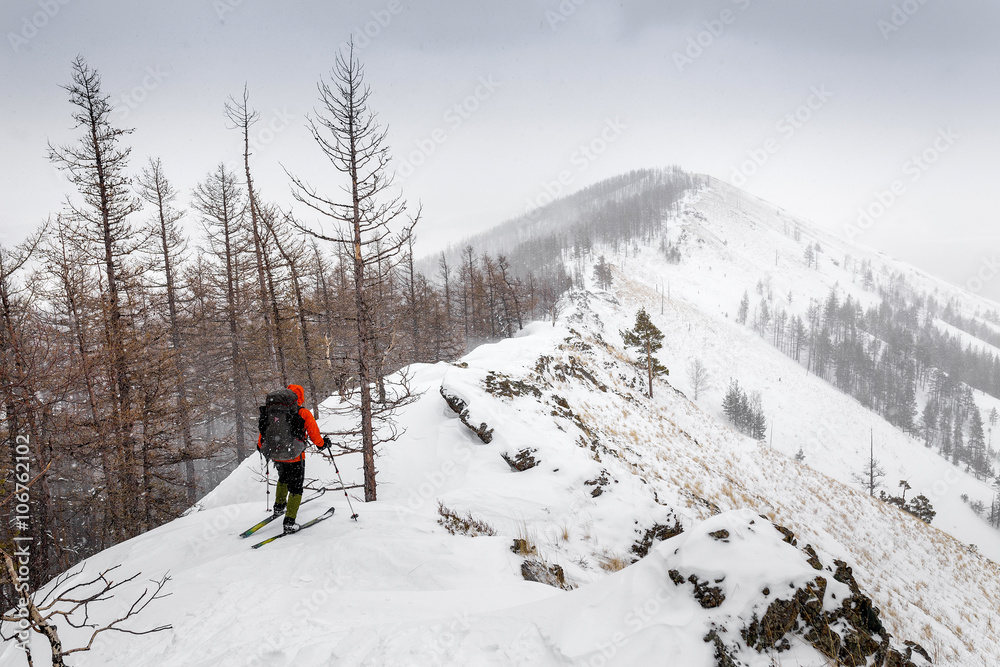 Man with skis and backpack standing on a trail at mountain top