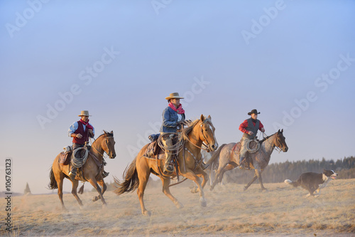 USA, Wyoming, three riding cowboys and a dog