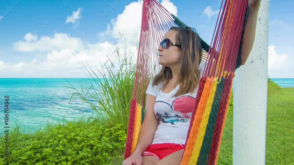 A Young Woman Swinging on a Colorful Hammock Overlooking a Turquoise Colored Ocean from a Tropical Island in Bermuda. Ultra High Definition, 4K