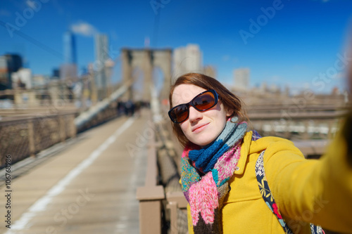 Beautiful young woman taking a selfie with her smartphone on Brooklyn Bridge, New York © MNStudio