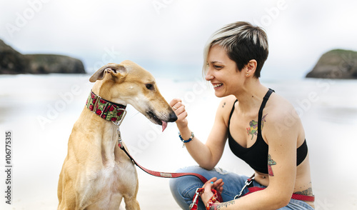 Spain, Llanes, smiling young woman with her greyhound on the beach photo