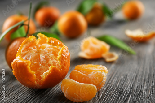 Peeled fresh tangerines with leaves and ripe mandarins on wooden table, closeup