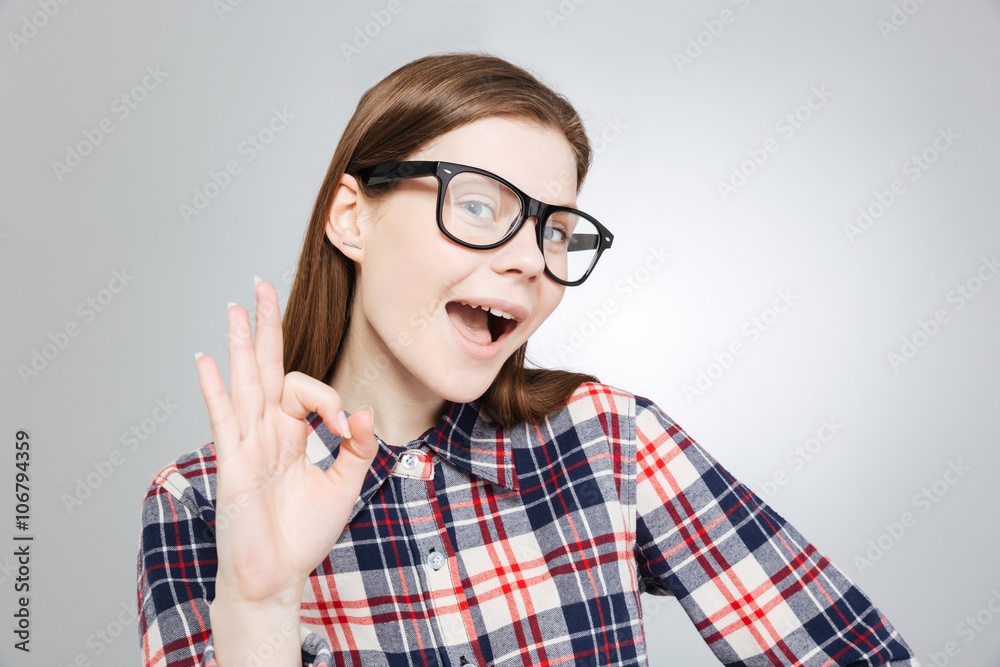 Happy charming teenage girl in glasses showing ok sign Happy charming teenage girl in glasses showing ok sign