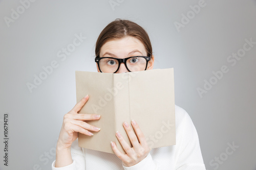 Wondered teenage girl in glasses covered face with book