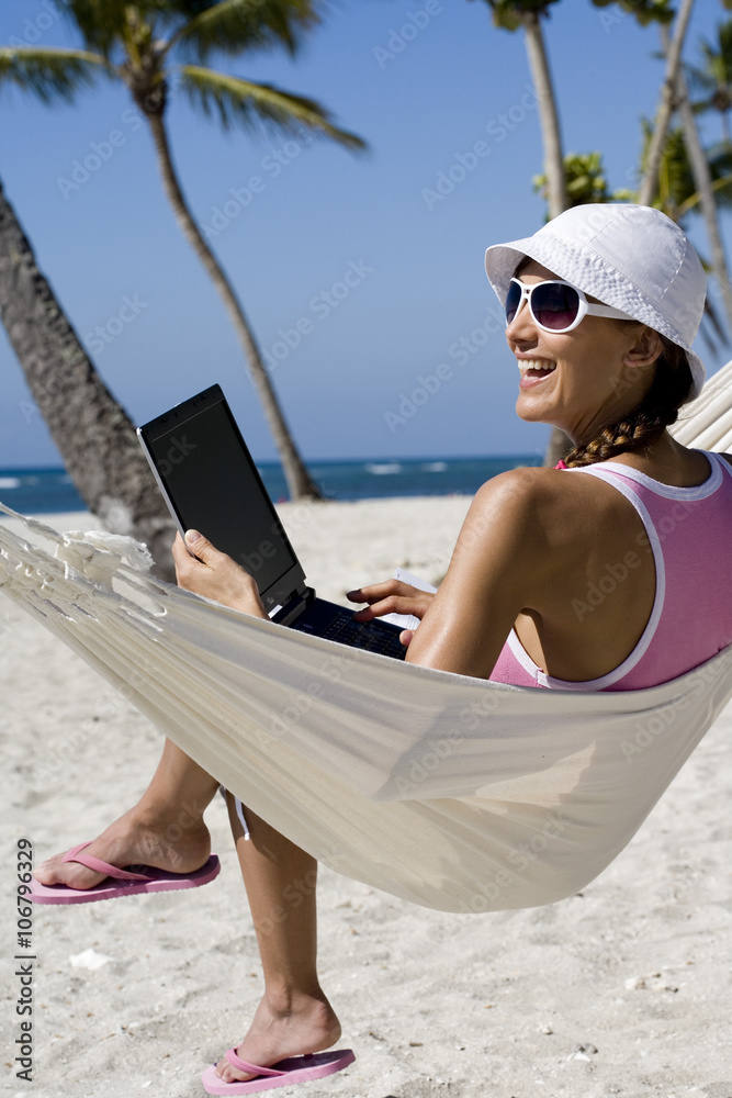 Naklejka premium femme souriant dans un hamac à la plage avec un ordinateur portable