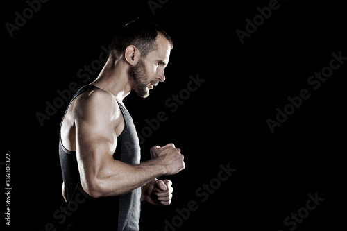 muscular man, clasps hands in fist, black background, place for text on the right