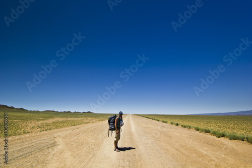 traveller with backpack on a lonely road in desert