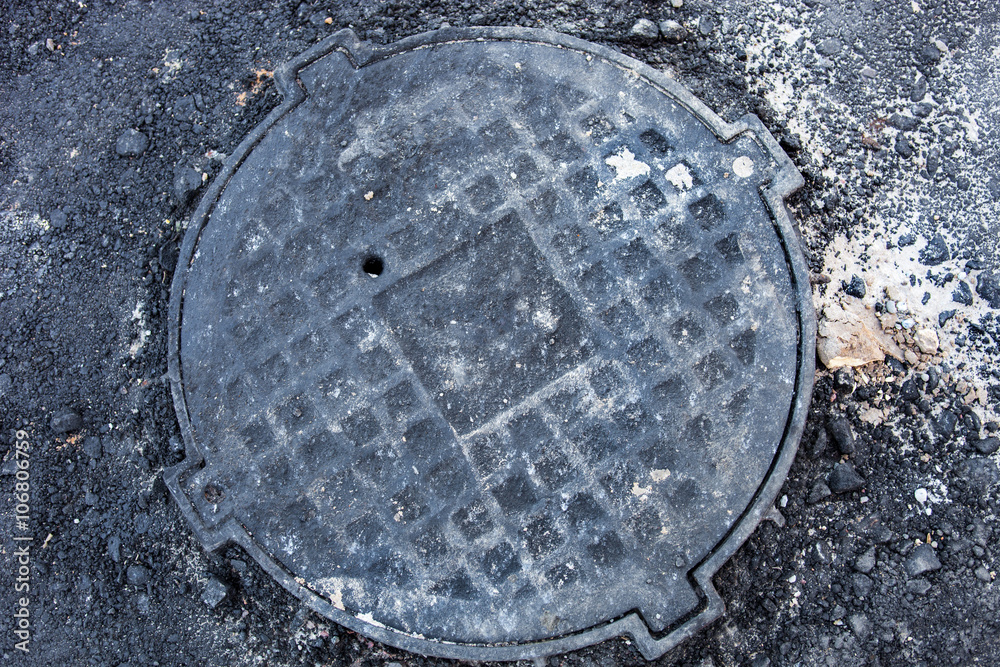Manhole with metal cover in asphalt surface Manhole with metal cover in asphalt surface