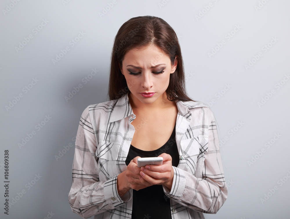 Worried unhappy young woman typing sms and looking on mobile pho