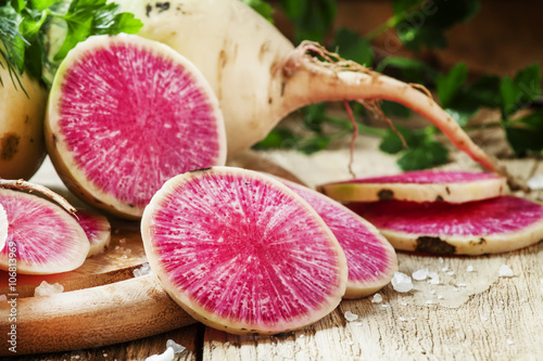 Slices of pink watermelon radish on a wooden table with parsley