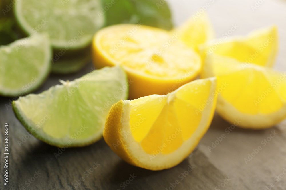 Slices of fresh lemon and lime with green leaves on table closeup Slices of fresh lemon and lime with green leaves on table closeup