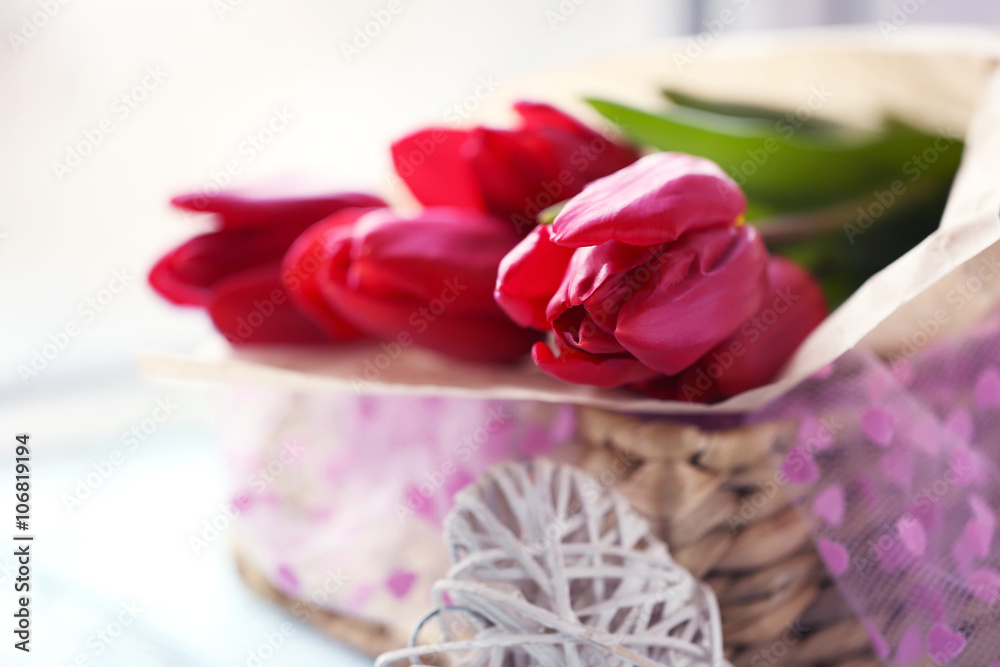 Red tulips in a wicker basket on a light-blue table