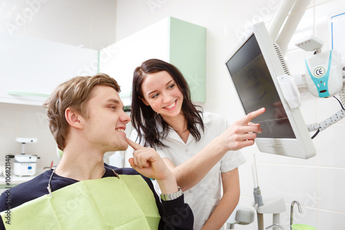 Young man on a review of a dentist, sitting in a chair. Dentist Explaining X-Ray on computer for patient in a dental clinic