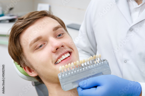 Close up portrait of Young man in dentist chair, Check and select the color of the teeth. Dentist makes the process of treatment in dental clinic office