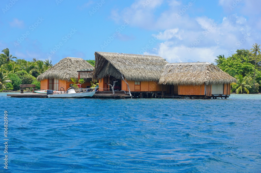 Tropical home over water with thatched roof and a boat at dock, Huahine island, Pacific ocean, French Polynesia Tropical home over water with thatched roof and a boat at dock, Huahine island, Pacific ocean, French Polynesia