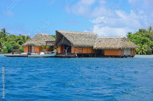Tropical home over water with thatched roof and a boat at dock, Huahine island, Pacific ocean, French Polynesia