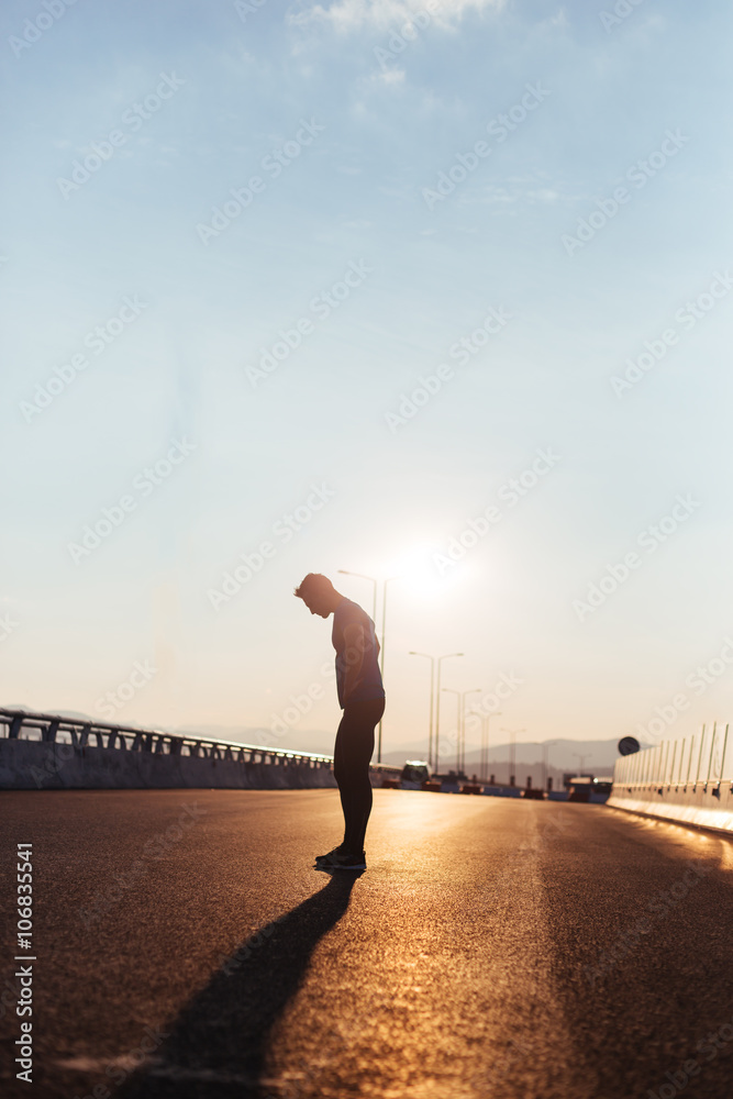 Fototapeta premium Attractive fit man running along big modern bridge at sunset lig