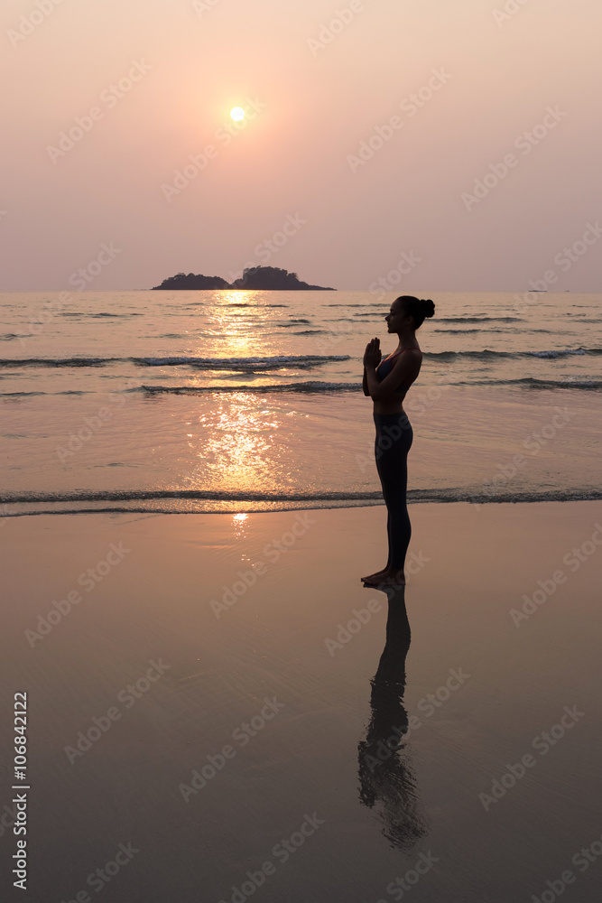 Young slim woman practicing pose from yoga on the beach at sunse