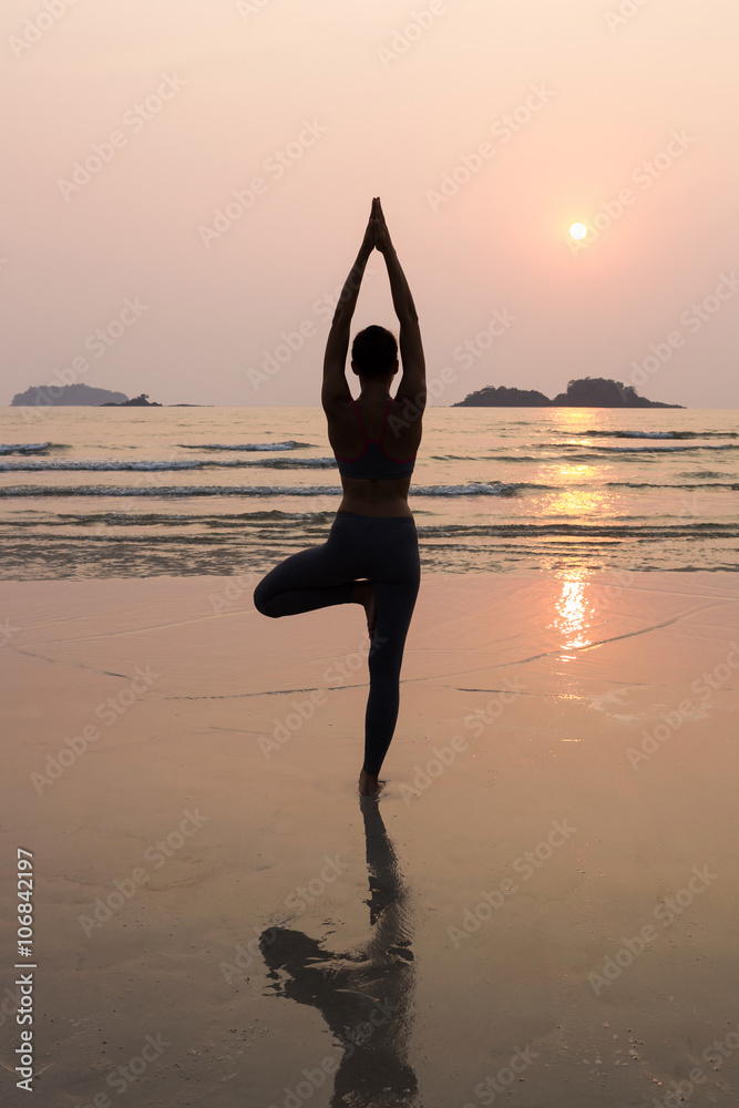 Young slim woman practicing pose from yoga on the beach at sunse