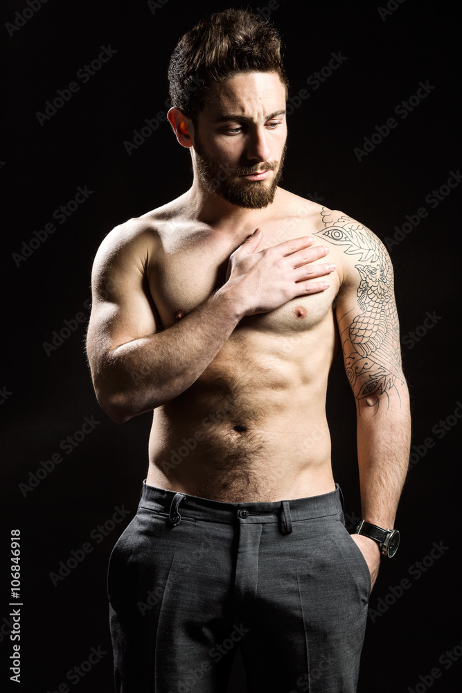 Fototapeta premium Handsome young man with tattoos posing. Isolated on black.