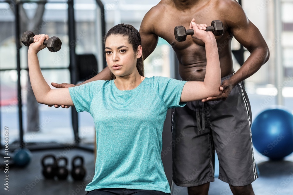 Athletic woman lifting weights helped by trainer