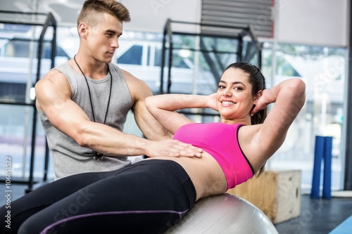 Male trainer assisting woman with sit ups