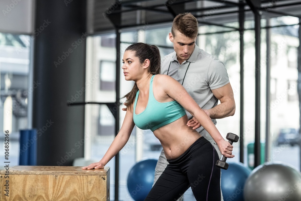 Fototapeta premium Male trainer assisting woman lifting dumbbells