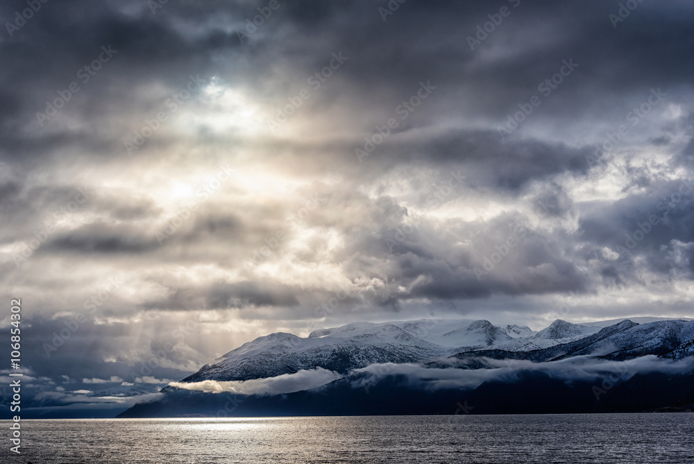 Snow caped mountains in norweigian fjord, with fog and low hanging storm clouds