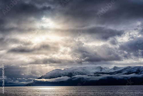 Snow caped mountains in norweigian fjord, with fog and low hanging storm clouds