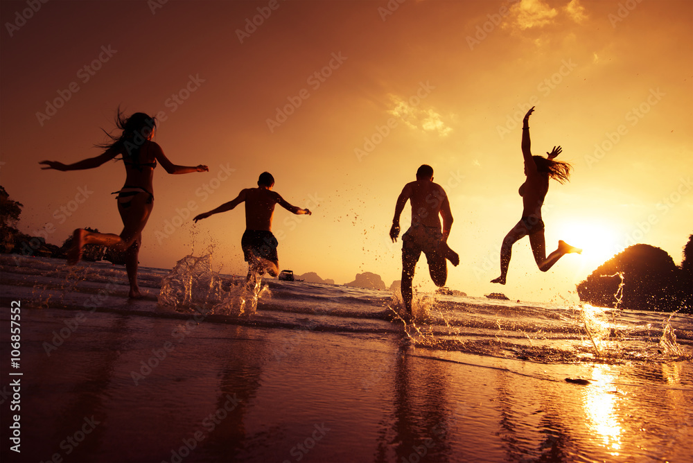 Fototapeta premium Group of happy young people is running on background of sunset beach and sea