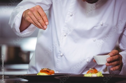 Chef sprinkling spices on dish in commercial kitchen