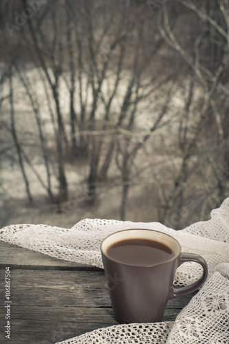 Cup of black coffee in front of the window and lace on wooden background.