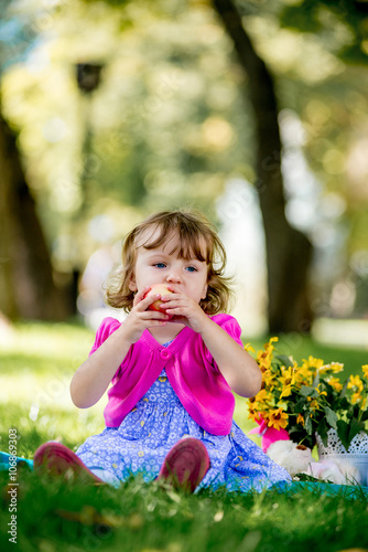 Cute little girl eating apple in the park