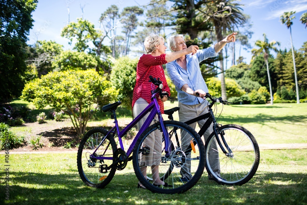 Senior couple standing with bicycle in park Senior couple standing with bicycle in park