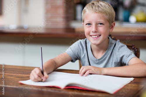 Portrait of happy boy doing homework in kitchen photo