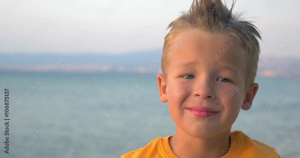 Close-up shot of a little cute boy with mohawk hair-do smiling. Portrait against blue sea and sky background Close-up shot of a little cute boy with mohawk hair-do smiling. Portrait against blue sea and sky background
