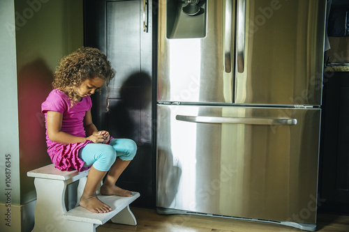 Sad mixed race girl sitting near refrigerator photo