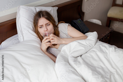 Unhappy sick girl lying on bed drink water from glass