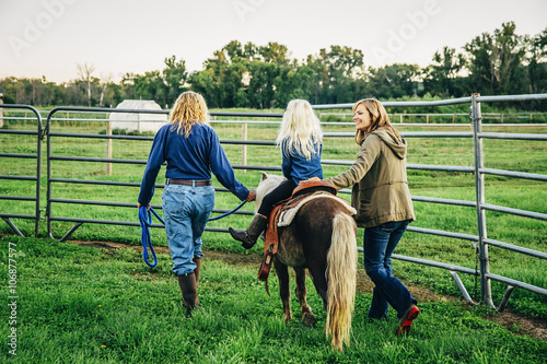 Three generations of Caucasian women walking miniature horse on farm