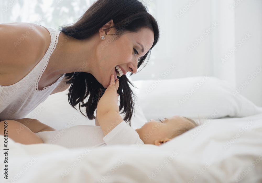 Mixed race mother playing with baby on bed Mixed race mother playing with baby on bed