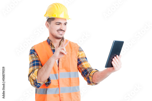 Smiling constructor using tablet and showing peace or victory ge