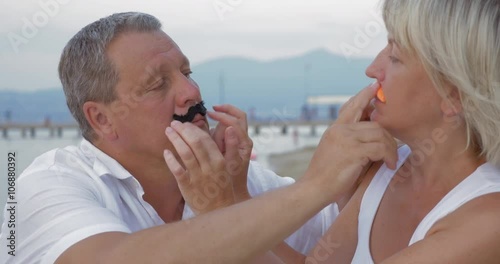 Mature couple is having fun, they are sticking false moustaches to each other and pulling faces.
