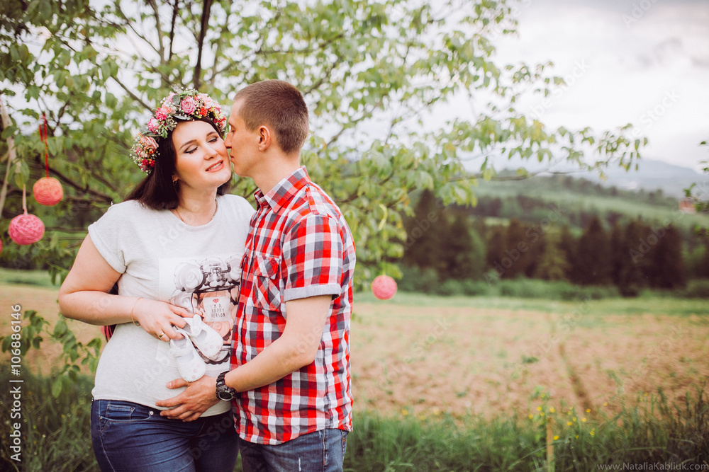 Pregnant woman in blue jeans and a T-shirt with her husband on the mountains background. Future parents Pregnant woman in blue jeans and a T-shirt with her husband on the mountains background. Future parents